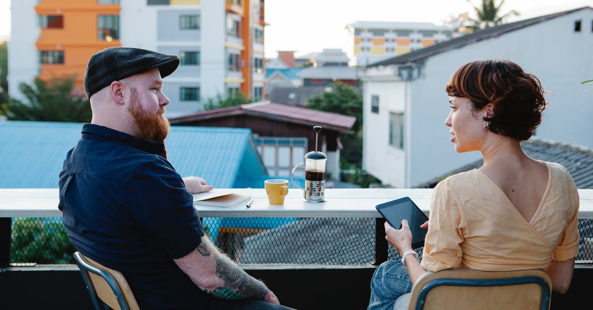 Is there any city now that has portals to all the other cities? - Back view of young woman with tablet and stylish man resting with cup of coffee in terrace in daytime