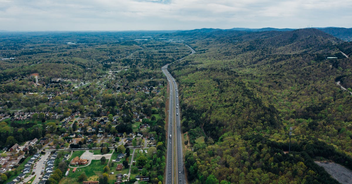 Is there any way a captured but non-ceded city can grow again? - Drone view of narrow wavy asphalt road with driving cars surrounded by lush green trees and parked vehicles in town under sky with horizon line