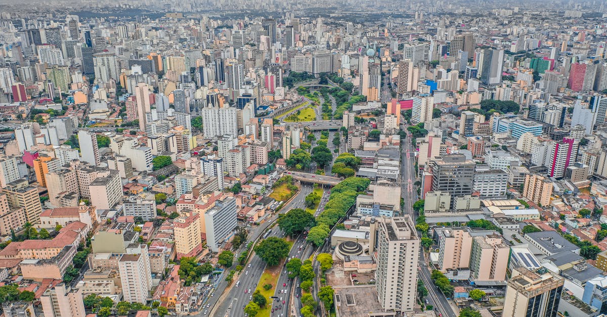 Is there any way a captured but non-ceded city can grow again? - Drone view of tall contemporary residential houses located on streets of modern city with asphalt road and lush green trees