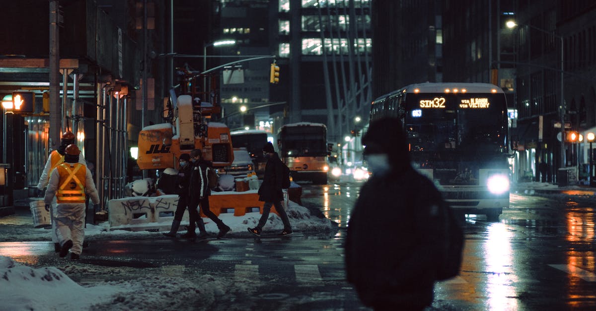 Is there any way to get snow layers to light up properly? - People in medical masks strolling on crosswalk near roadway with glowing buses on dark street during winter evening in city