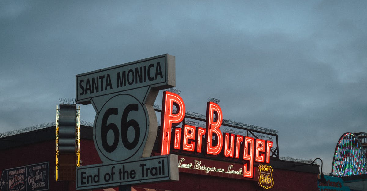 Is there any way to increase the text size? - Low angle of road sign with Route 66 End of the Trail inscription located near fast food restaurant against cloudy evening sky on Santa Monica Beach
