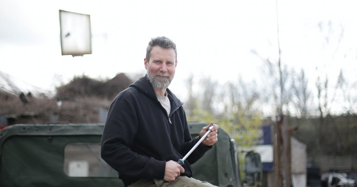 Is there anyway to refill a repair tool outside of a garage? - Side view of smiling middle aged man in black hoodie sitting on metal trunk of car outside garage and looking at camera