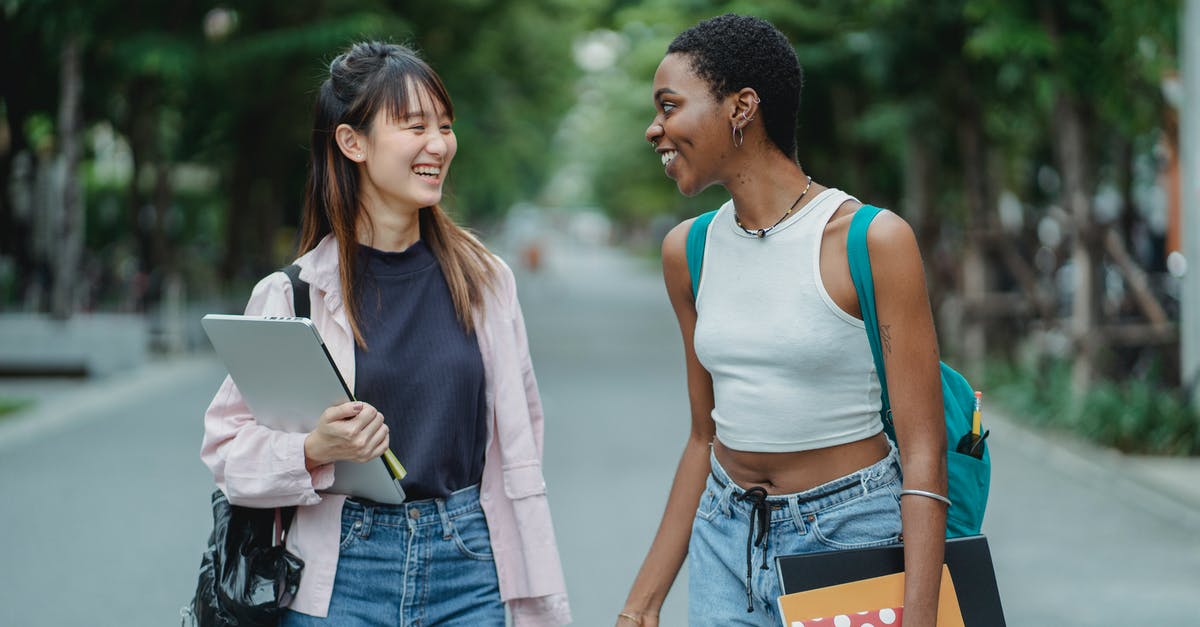 Is there no other way to remove the "7 day purchase" market ban other than spending money? - Smiling young multiethnic women standing in middle of street with laptop and notebooks while speaking with each other in summer day and wearing casual clothes while looking at each other