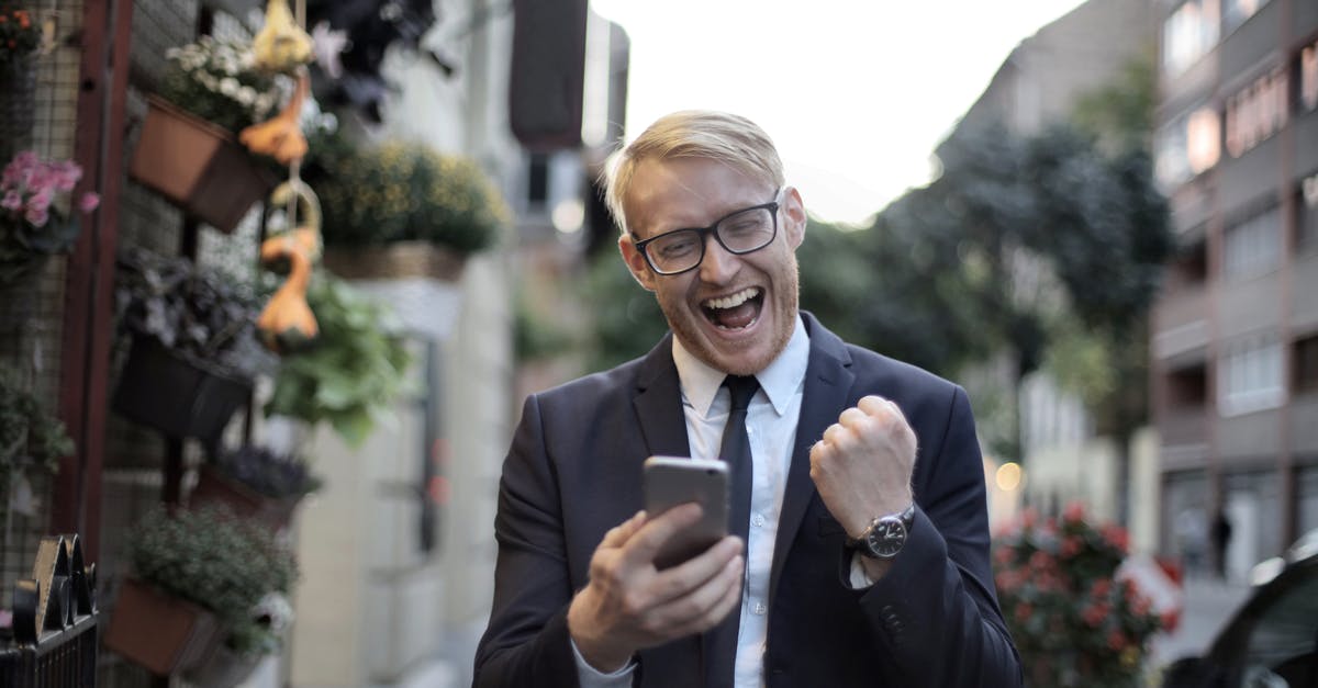 Is using Steam Achievement Manager (SAM) against Steam rules? - Excited young man in formal wear and eyeglasses clenching fist and rejoicing victory while using mobile phone in modern city street