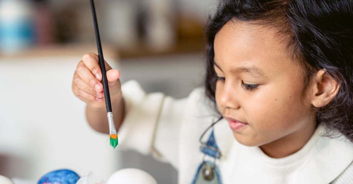 Is what is inside of an Egg Pre-Determined? - Side view of concentrated Hispanic girl with paintbrush painting white eggs during Easter preparation in light room on blurred background