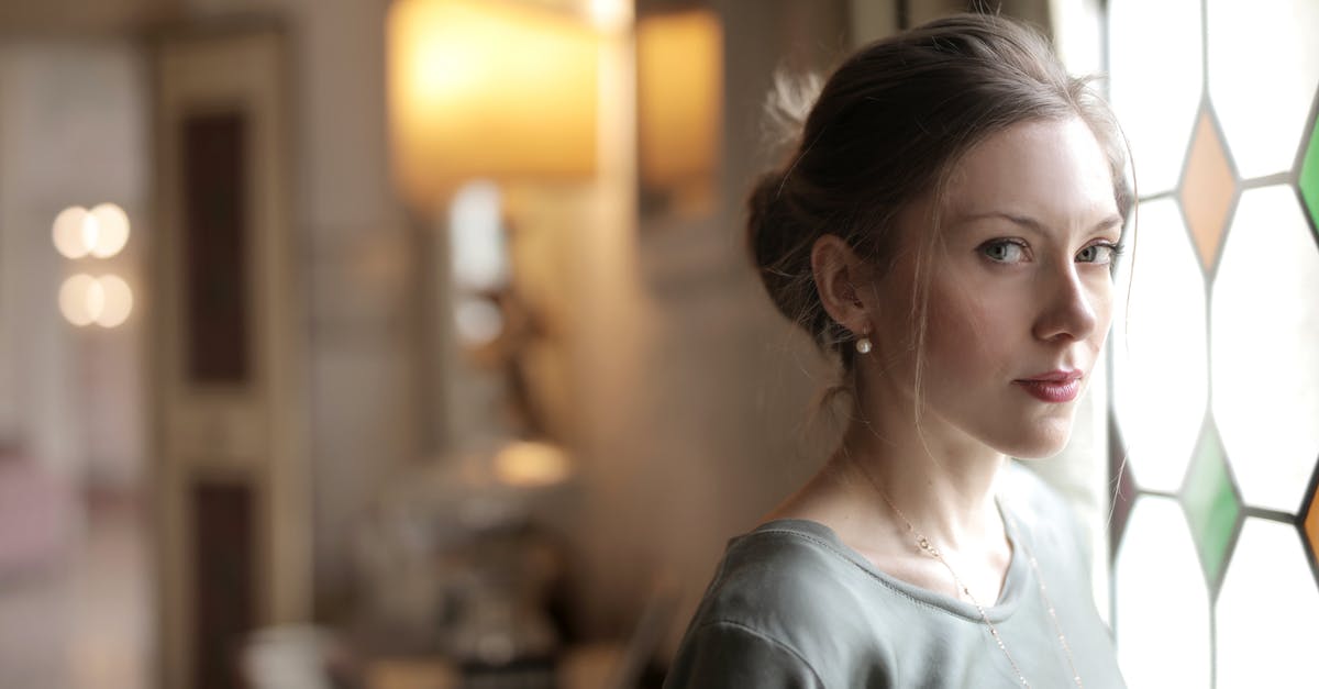 Item and ability visit on the same person - Pretty casual serious lady with hairstyle intently looking at camera while standing near stained glass window in bright luxury room of old mansion