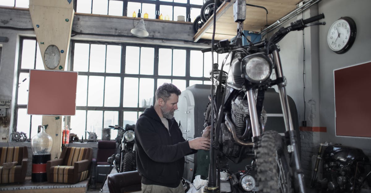 Jamie the robot repair and use - Side view of bearded adult mechanic in casual uniform standing near motorcycle and working with engine in workshop Jamie the robot repair and use - Side view of bearded adult mechanic in casual uniform standing near motorcycle and working with engine in workshop