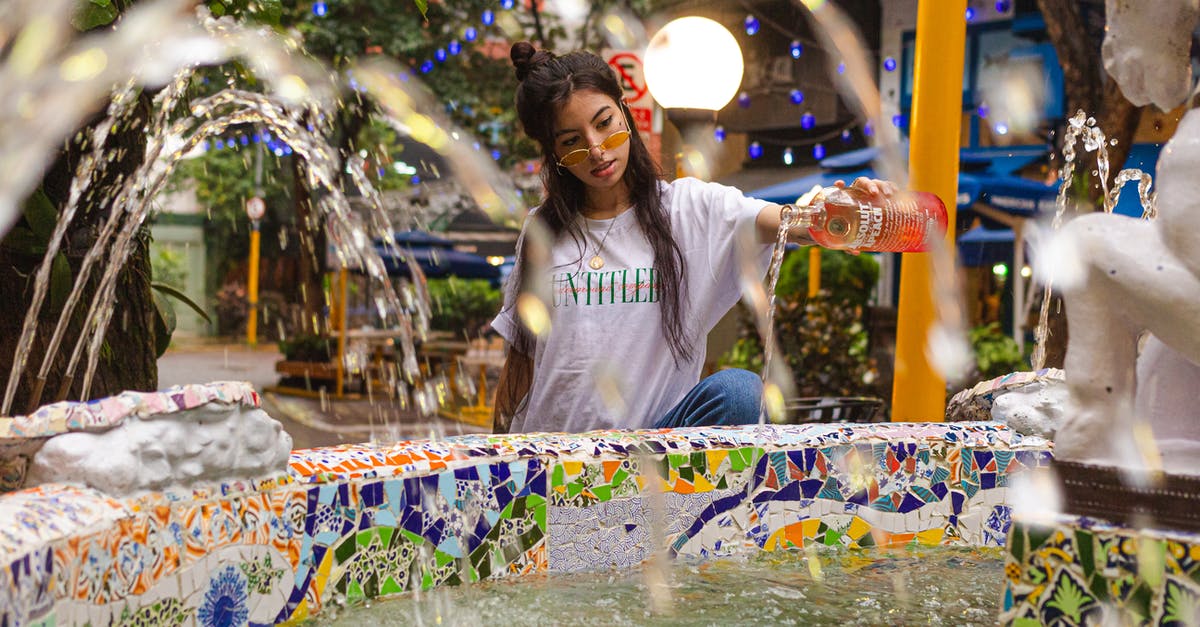 (Java Minecraft 1.13) How to summon a splash water bottle with no gravity? - Trendy female in sunglasses pouring alcohol drink from bottle into colorful fountain with jets of water while standing on decorated street with building