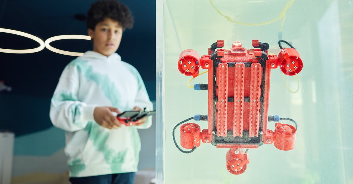 Joystick dead zone with flight simulators - From below of ethnic boy in hoodie controlling robot using panel while standing in light room