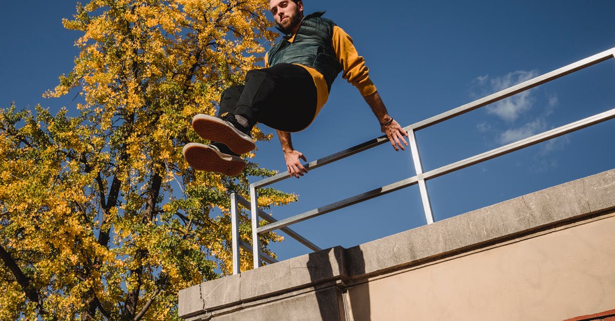 Judging Uruk Captain strength / level: How high is too high? - From below of active male jumping from fence on top of building during parkour training against blue sky and tree on street Judging Uruk Captain strength / level: How high is too high? - From below of active male jumping from fence on top of building during parkour training against blue sky and tree on street