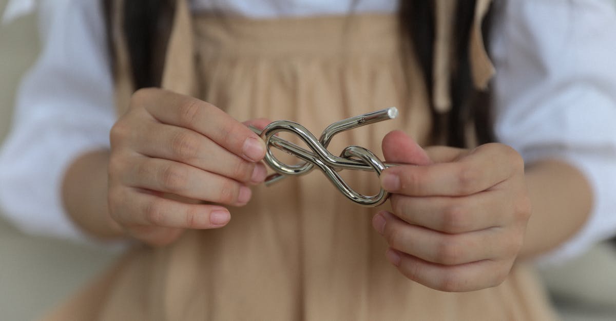 Jurassic World the Game age problem - Crop anonymous child in casual wear holding metal wire brain teaser in shape of knot while playing at home Jurassic World the Game age problem - Crop anonymous child in casual wear holding metal wire brain teaser in shape of knot while playing at home