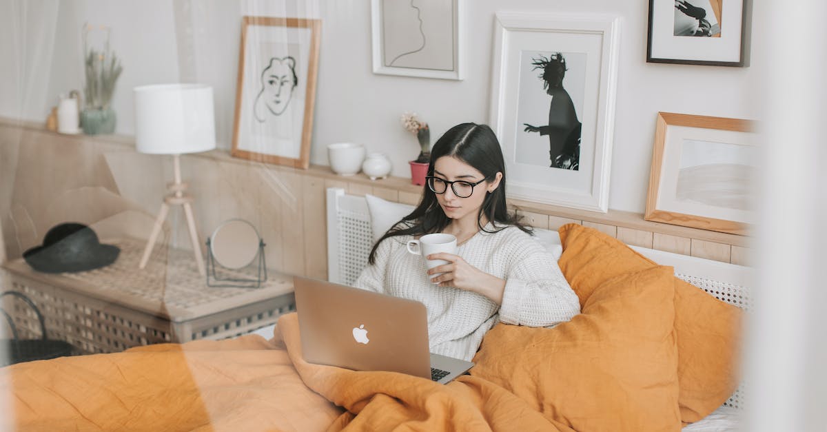 KOTOR 2 Freezes on Movies - Focused young brunette in eyeglasses with cup of hot drink lying in comfortable bed and working on laptop in morning