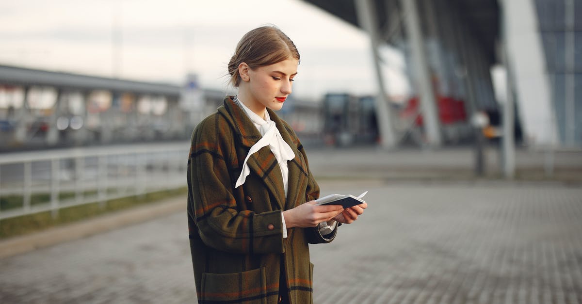 League of Explorers ticket dates - Attentive female passenger wearing trendy plaid coat and white blouse checking passport and ticket standing on pavement near modern building of airport outside