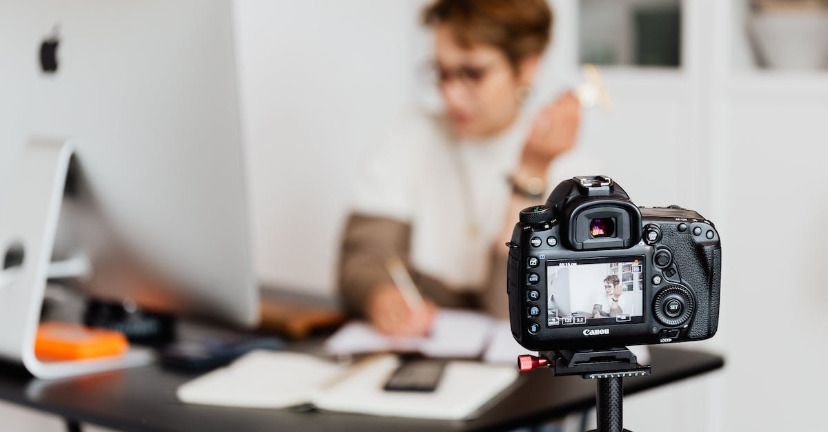 Leaping shot op in Online mode? - Unrecognizable blurred lady working at table in modern office against photo camera placed on tripod Leaping shot op in Online mode? - Unrecognizable blurred lady working at table in modern office against photo camera placed on tripod