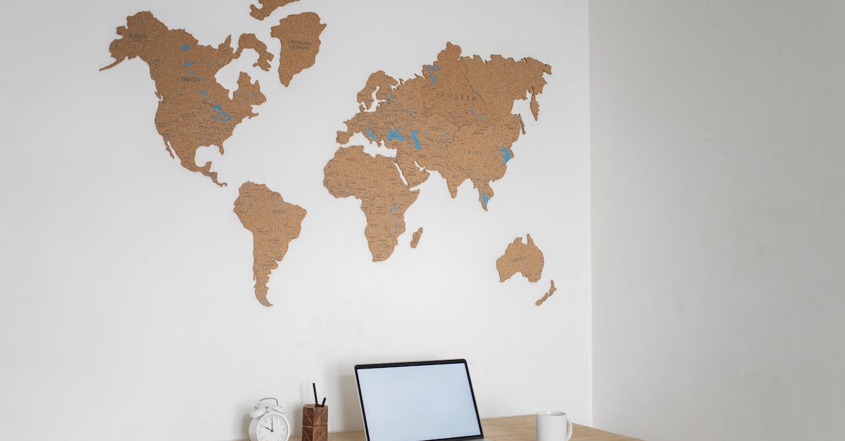 Load world from PC to PE [duplicate] - Wooden table with modern netbook with blank screen and alarm clock placed at white wall with decorative world continents in light room