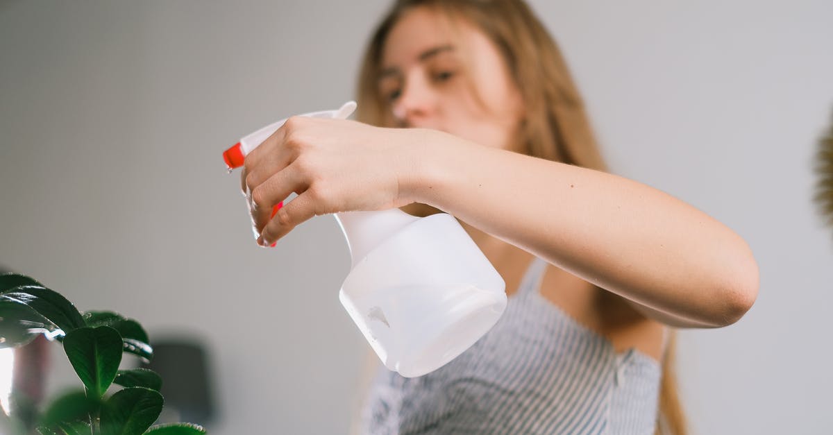 Long-distance fluid handling with pipes - Long haired lady using white spray bottle for green plant in selected focus Long-distance fluid handling with pipes - Long haired lady using white spray bottle for green plant in selected focus