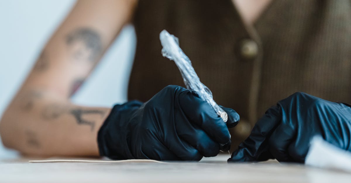 Machine Guns or Cannons? - Crop anonymous artist in black gloves drawing with tattoo machine on practice skin on blurred background