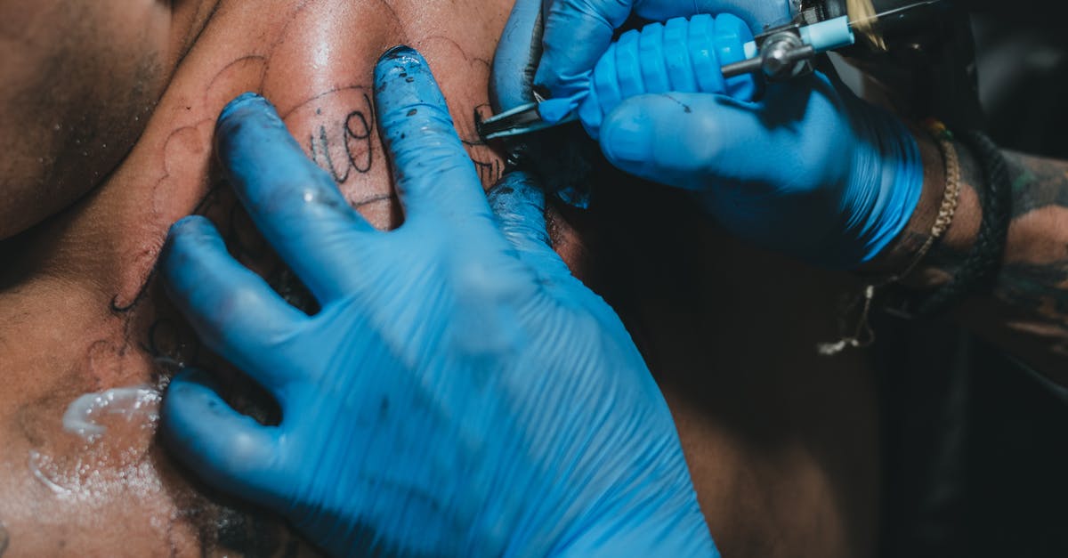 Make Guns Available? - High angle hands of anonymous tattooist in blue gloves using professional tool to make tattoo on back of client in salon