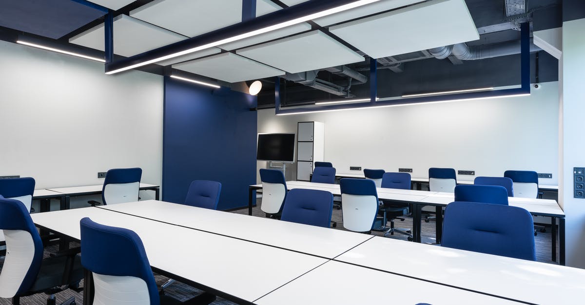 Make squad open to public - Interior of modern spacious workspace with long white tables and blue armchairs placed near monitor with black screen in business center Make squad open to public - Interior of modern spacious workspace with long white tables and blue armchairs placed near monitor with black screen in business center