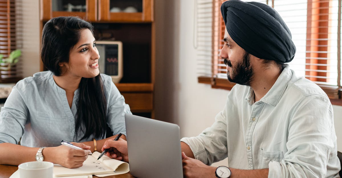 Make Trashcan Carla friendly again using commands - Indian male in turban and wristwatch typing on netbook while interacting with happy female coworker with notebook and pen sitting at table in office and looking at each other