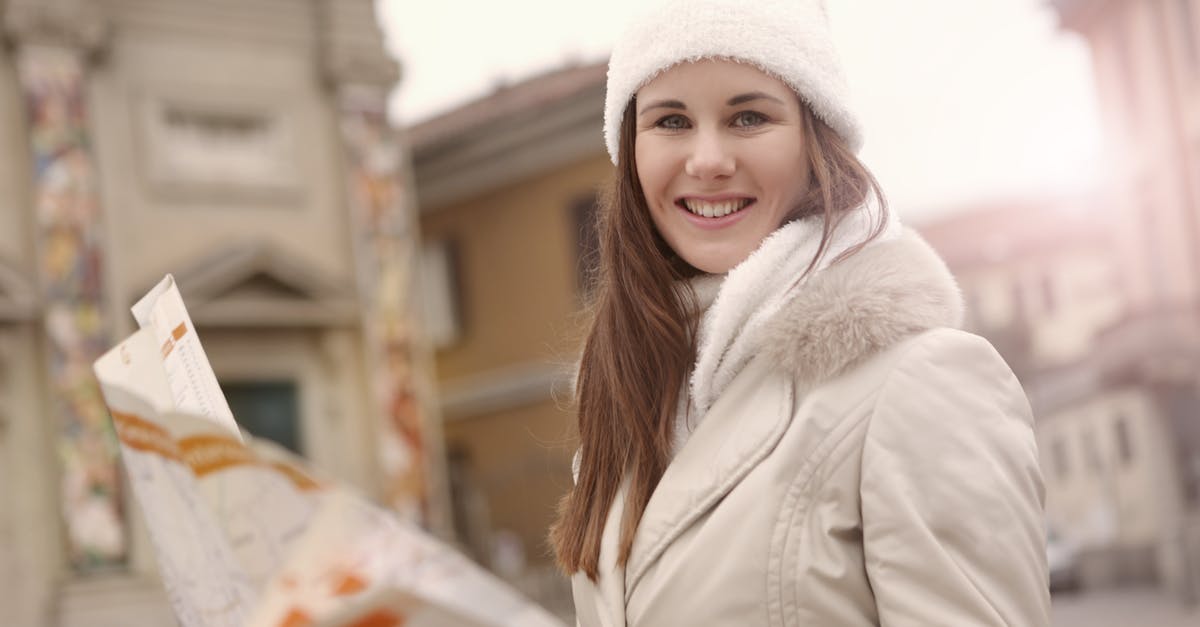 Mercer's Plans seem to appear outside of a map - Young female tourist in warm jacket hat and scarf holding paper map and looking at camera while standing in historical center of city