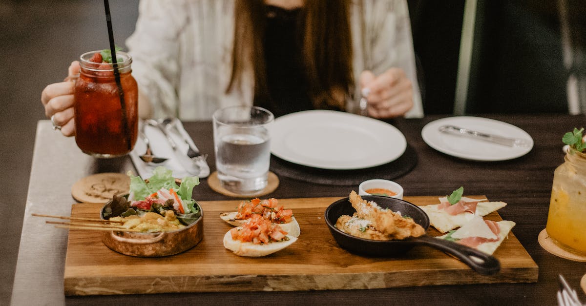 Merge Starter and Standard Edition? - Crop unrecognizable female in casual clothes having dinner in Asian restaurant while sitting at table with berry mocktail and grilled meat on sticks served with tomato sandwiches and spring rolls