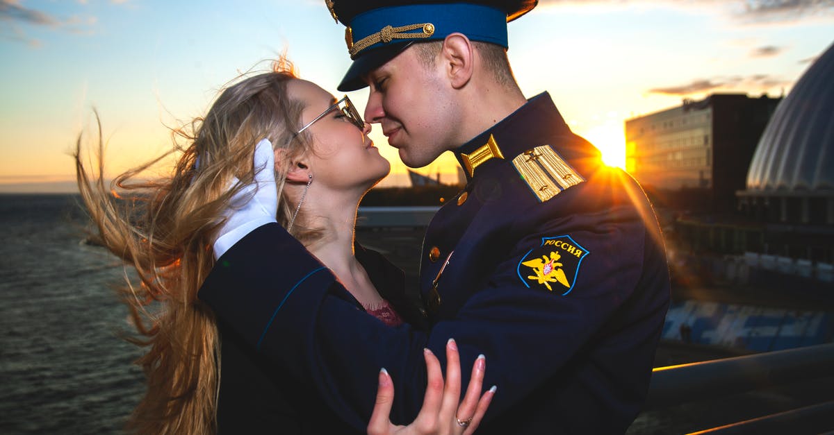 Military uprising and other problems in Tropico 5 - Side view of content military male embracing beloved in eyeglasses near fence and sea at bright sunset while looking at each other in back lit