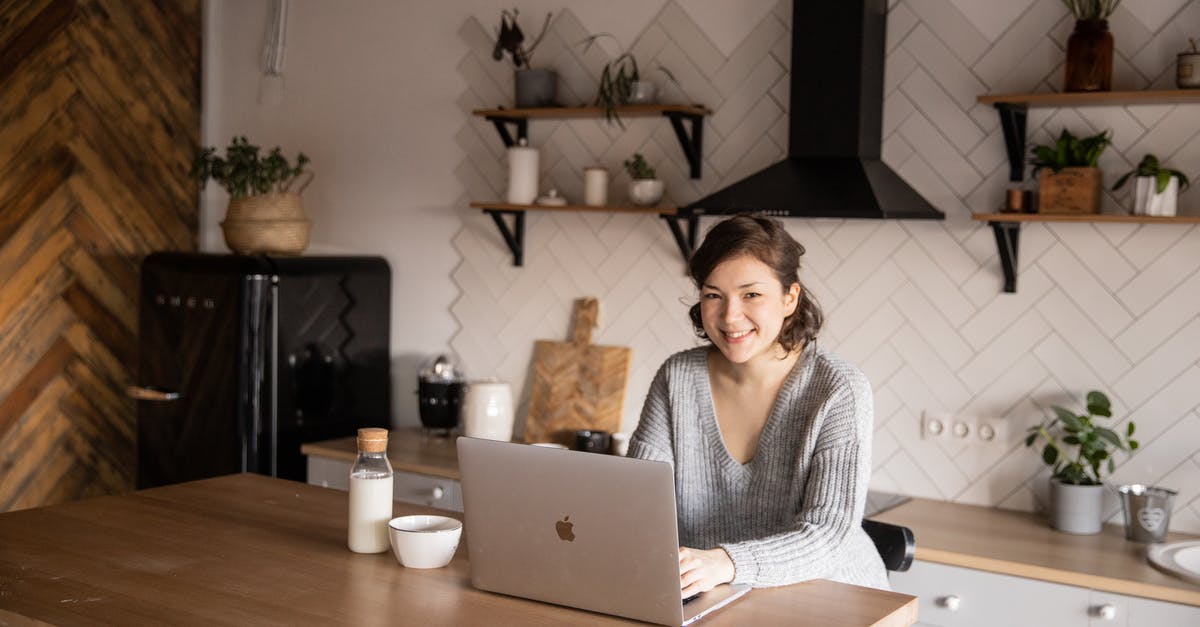 Minecraft: Using /execute to detect if a Bottle O' Enchanting has been thrown - Cheerful female in casual clothes sitting at table with laptop and bottle of milk while browsing internet on laptop during free time at home and smiling looking at camera