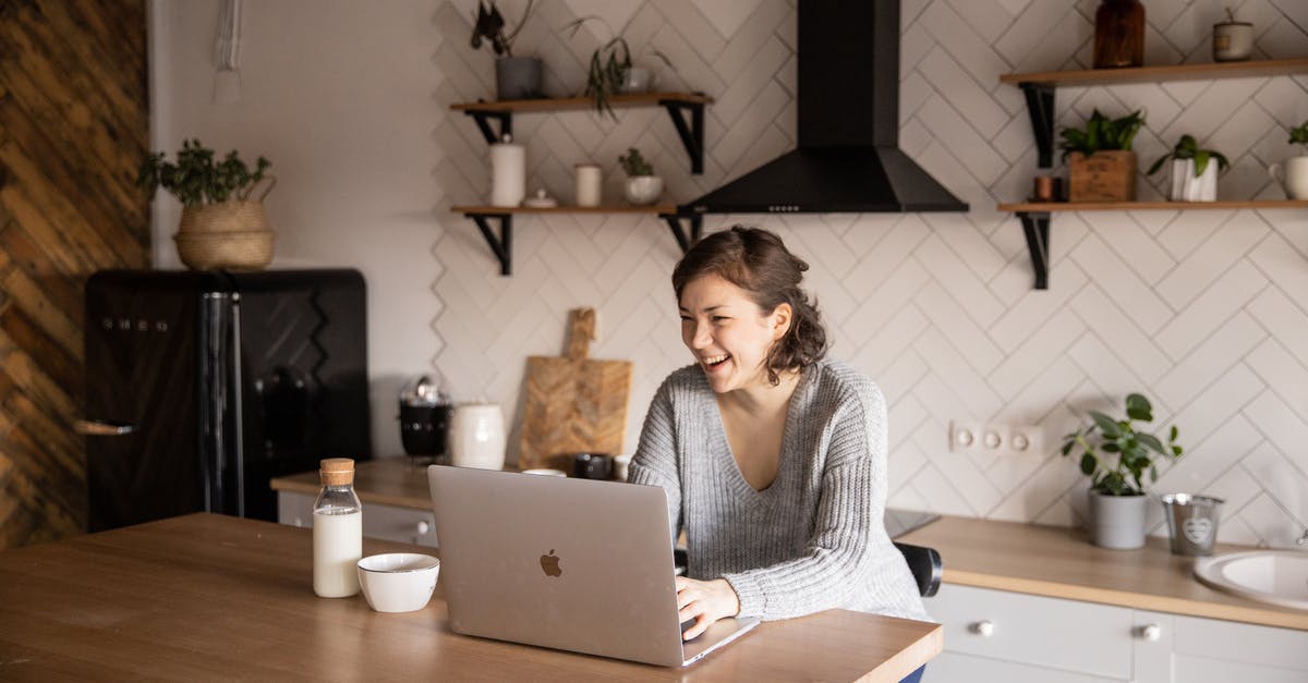 Minecraft: Using /execute to detect if a Bottle O' Enchanting has been thrown - Young female in gray sweater laughing while sitting at wooden table with laptop and milk bottle and having rest watching video during free time