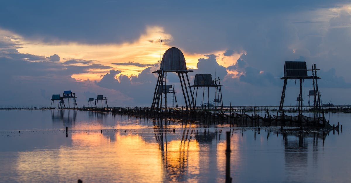Minimum support for elevated buildings - Elevated water tanks reflecting in glowing rippled lake under sky with fluffy clouds at sundown Minimum support for elevated buildings - Elevated water tanks reflecting in glowing rippled lake under sky with fluffy clouds at sundown
