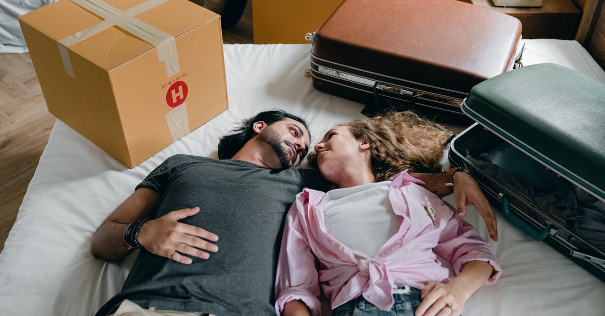 Mouse cursor won't move - From above of young ethnic bearded man and woman with curly hair looking at each other and lying on bed among suitcases and cardboard boxes with stuff while moving in new apartment together