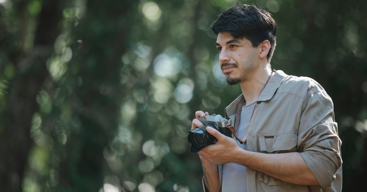 Multiplayer. Guy shoot at me. Misses. I die? - Focused bearded young male photographer in casual shirt with photo camera standing in woods and looking away