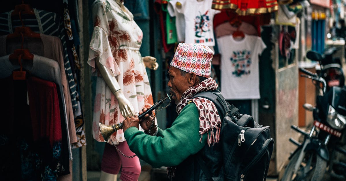 My Google Play Store is glitching so I can't download Minecraft - Side view of anonymous mature ethnic male artist with backpack playing musical instrument while standing in front of local clothing shop on city street in daylight near parked motorbike