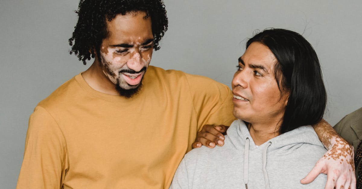 My Minecraft skin has been turned inside out - African American male with vitiligo skin hugging Native American colleague while browsing computer on gray background during remote work in studio