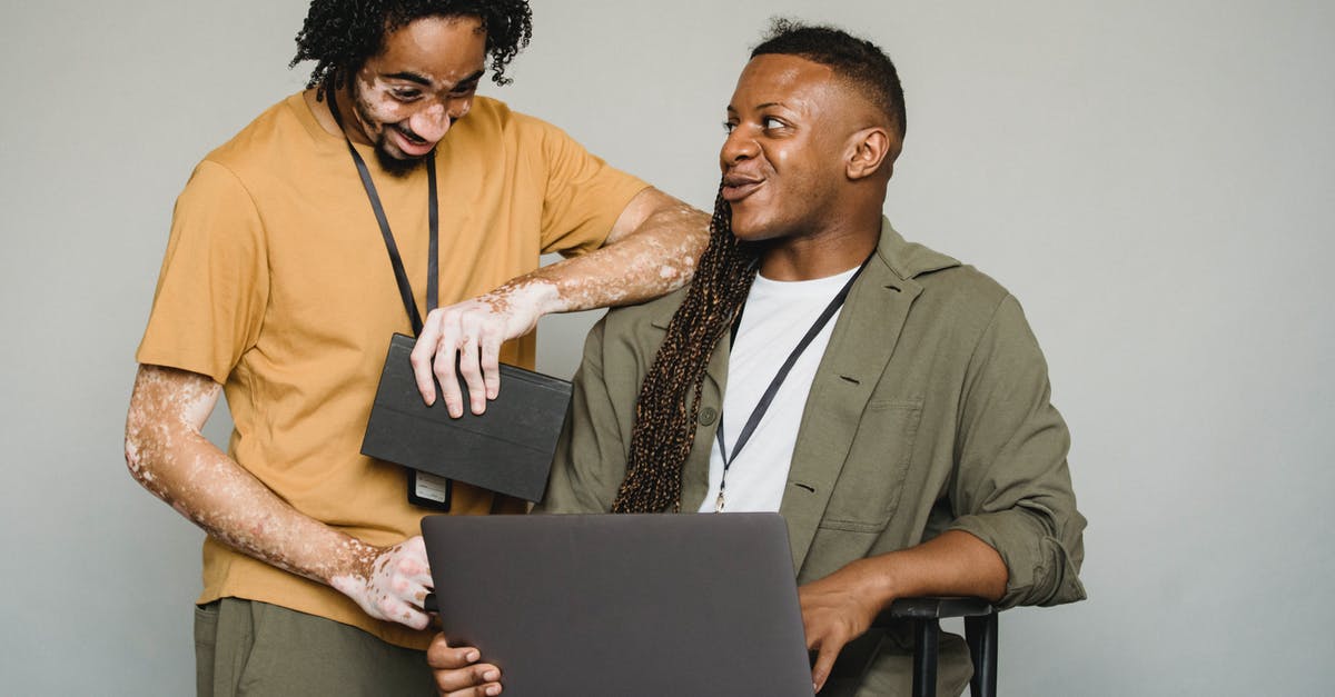 My Minecraft skin has been turned inside out - Happy African American androgynous person with Afro braids and computer looking at black colleague with vitiligo and notebook while working on gray background