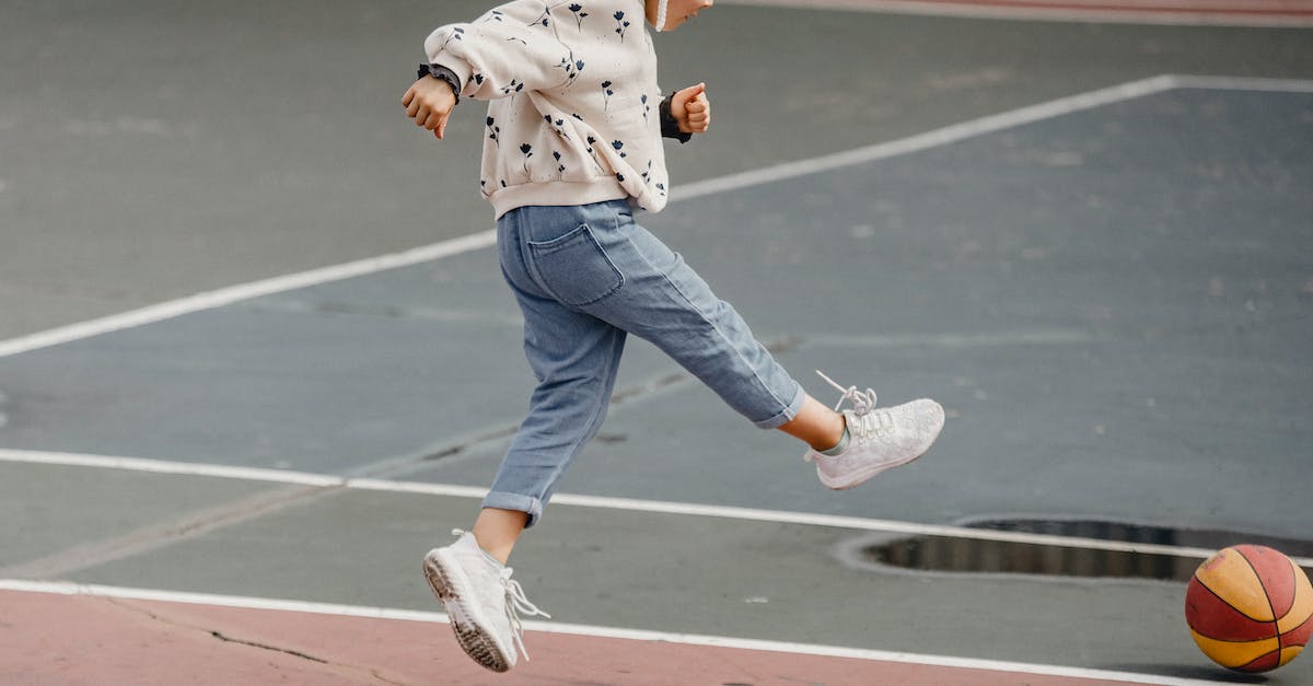 My player - View roster? - Side view of jumping little girl in jeans and jumper kicking colorful ball playing on sports yard