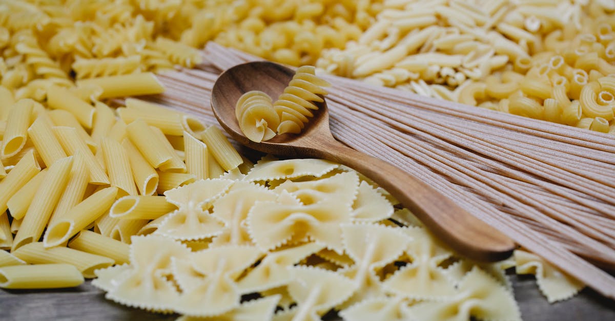 Name of the recipe for this type of wall? - Arrangement of uncooked various pasta including spaghetti fusilli farfalle and penne heaped on table with wooden spoon