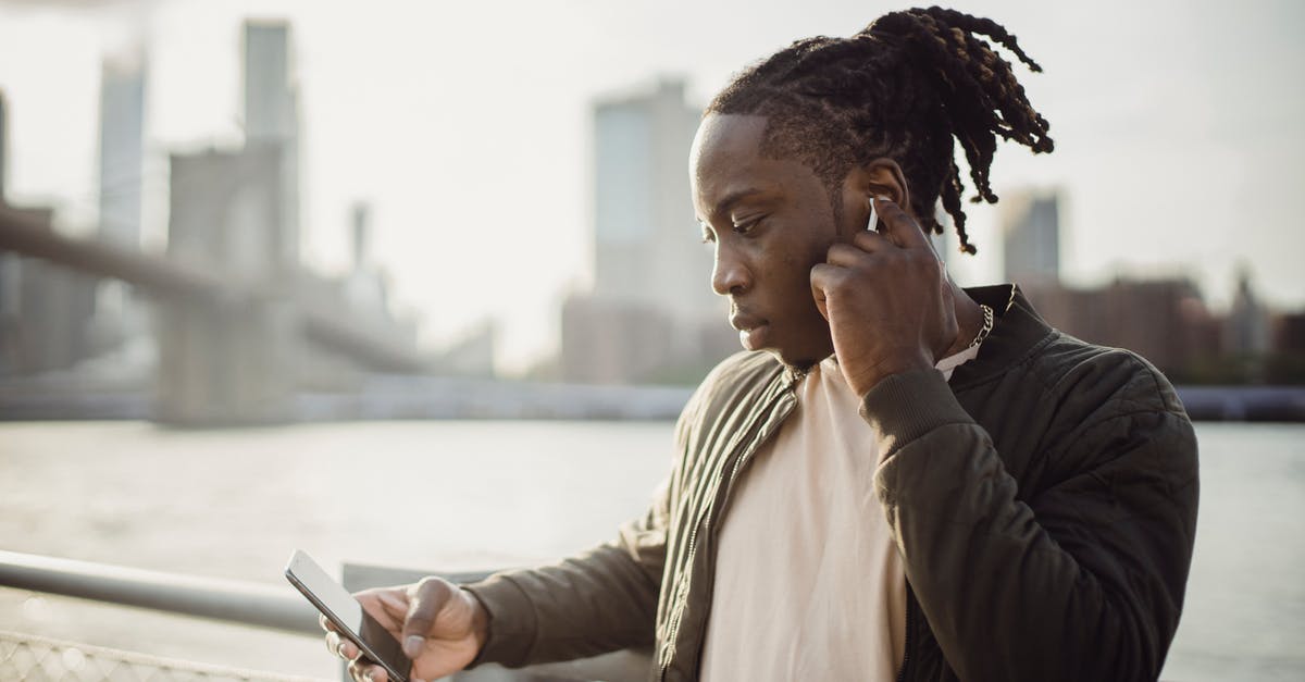 No Man's Sky - All Black Holes Created Equal? - Thoughtful adult African American guy in wireless earphones listening to music while surfing internet on cellphone and standing leaned on hand near fence on bridge over city river