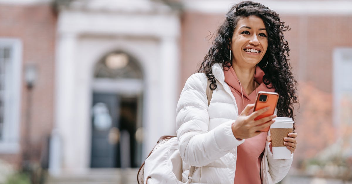 Notifications not going away - Cheerful young ethnic female student with long curly hair in casual clothes and backpack smiling and looking away while using mobile phone standing in campus with takeaway coffee Notifications not going away - Cheerful young ethnic female student with long curly hair in casual clothes and backpack smiling and looking away while using mobile phone standing in campus with takeaway coffee
