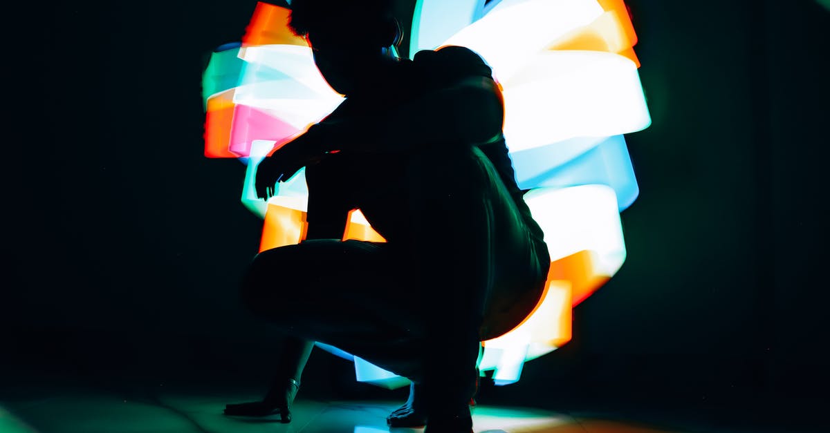 Obtaining Cloth in A Dark Room - Anonymous male in casual clothes squatting down near creative multicolored lights in dark room Obtaining Cloth in A Dark Room - Anonymous male in casual clothes squatting down near creative multicolored lights in dark room