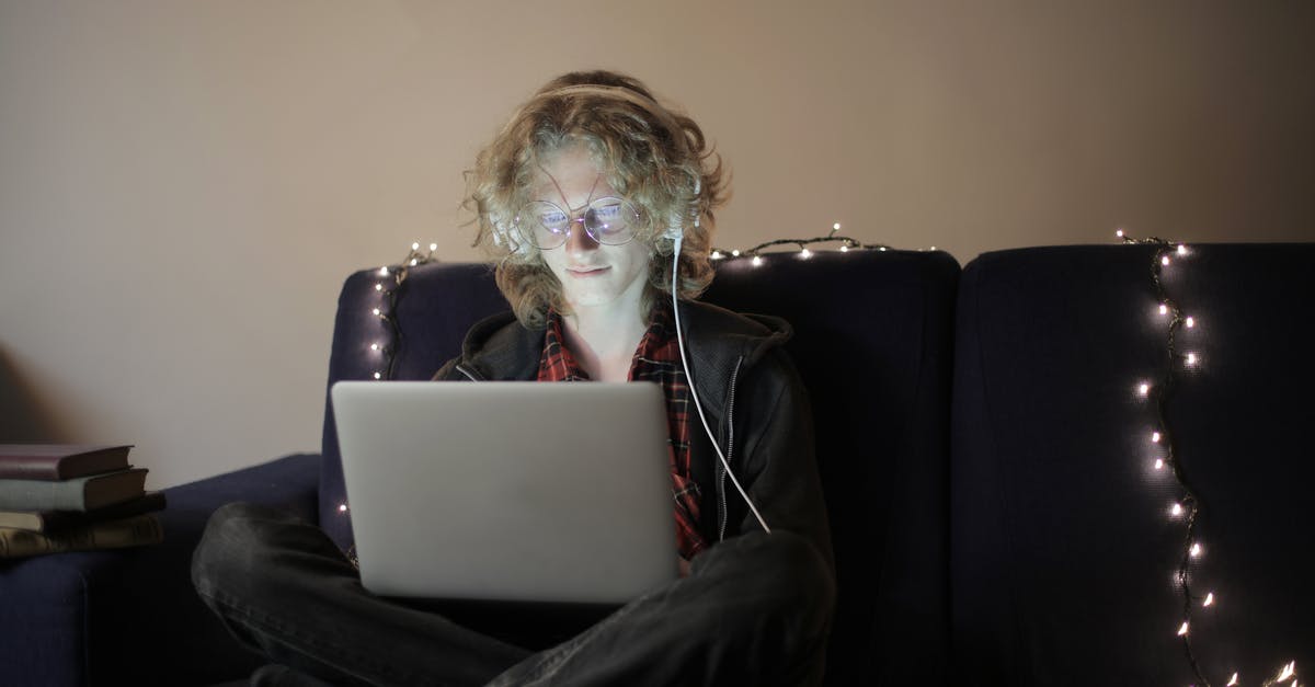 Offline even though network connection test passed - Enjoyable teen boy in casual outfit eyeglasses sitting on sofa with luminous garland browsing laptop and listening to music on headphones during evening at home