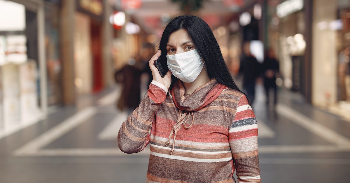Optimal all-around character builds - Worried casual female wearing protective mask and looking at camera while answering phone call against blurred background in city center during coronavirus pandemic