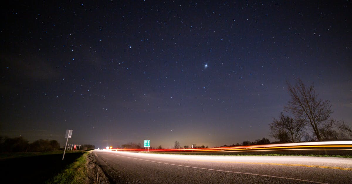 Optimal Magic Levels - From below of glowing asphalt road with fence near trees and road signs under picturesque night sky with luminous stars at sundown