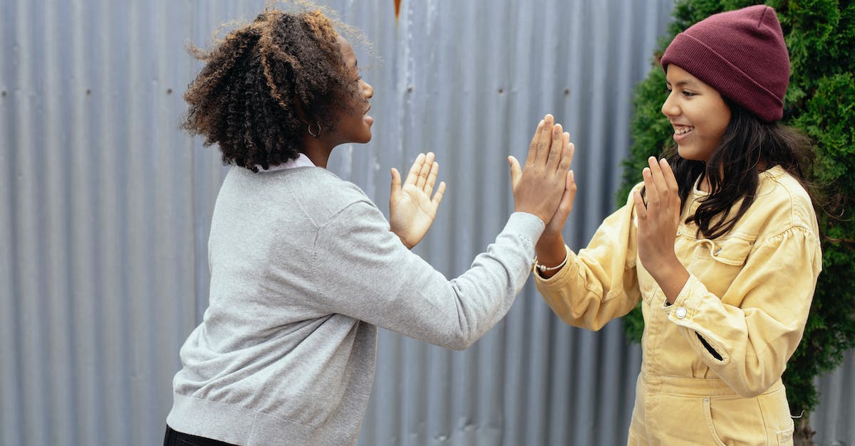 Other users play the games? - Side view of happy multiracial schoolgirls standing near metal fence while playing game with hands and looking at each other Other users play the games? - Side view of happy multiracial schoolgirls standing near metal fence while playing game with hands and looking at each other