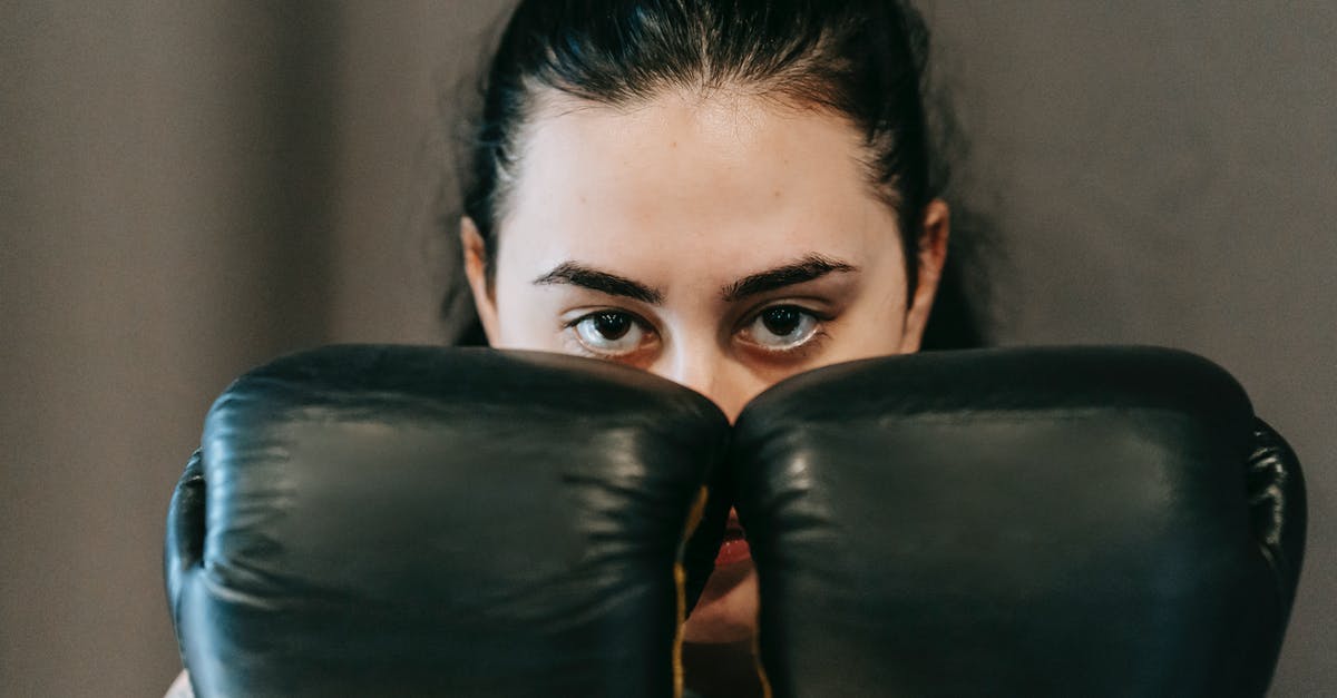 Physical resistance vs. Armor vs. Defence - Concentrated young female athlete with long dark hair covering face with hands in boxing gloves during training Physical resistance vs. Armor vs. Defence - Concentrated young female athlete with long dark hair covering face with hands in boxing gloves during training