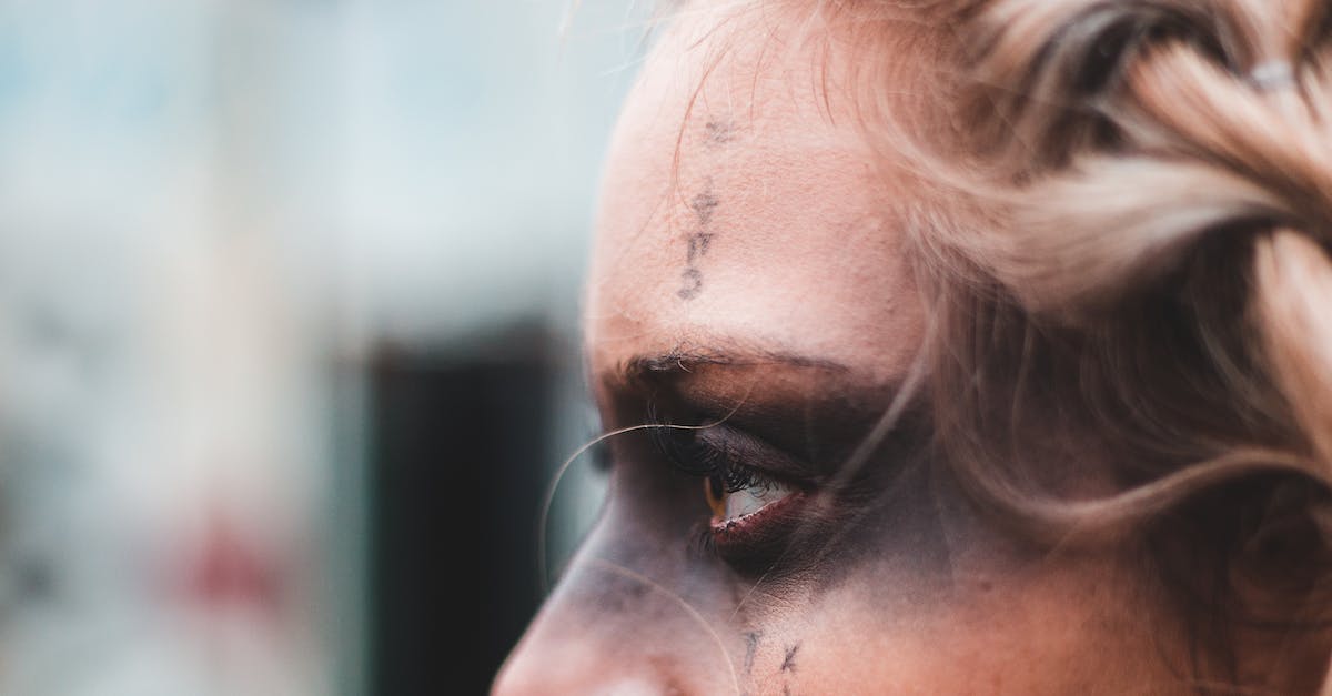 Piercing or Critical For Magic Attacks? - Crop side view of blond woman with black mask makeup and symbols on face looking away Piercing or Critical For Magic Attacks? - Crop side view of blond woman with black mask makeup and symbols on face looking away