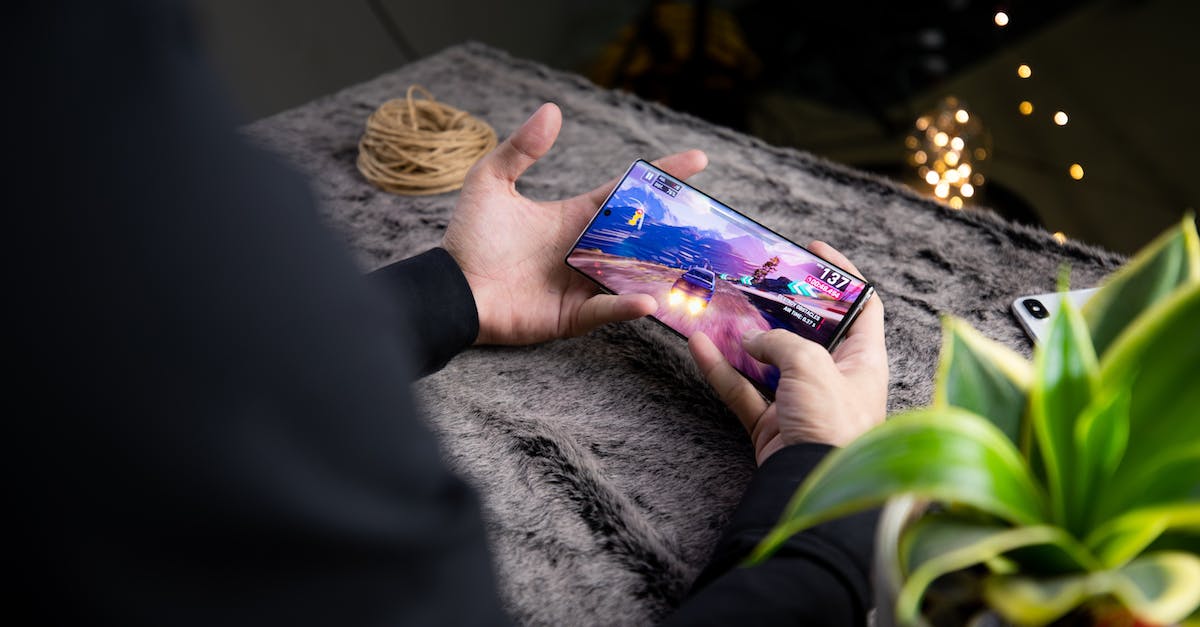 Play a specific mission over in Mass Effect 3 - From above of crop anonymous person playing video game on modern cellphone with image of car on screen