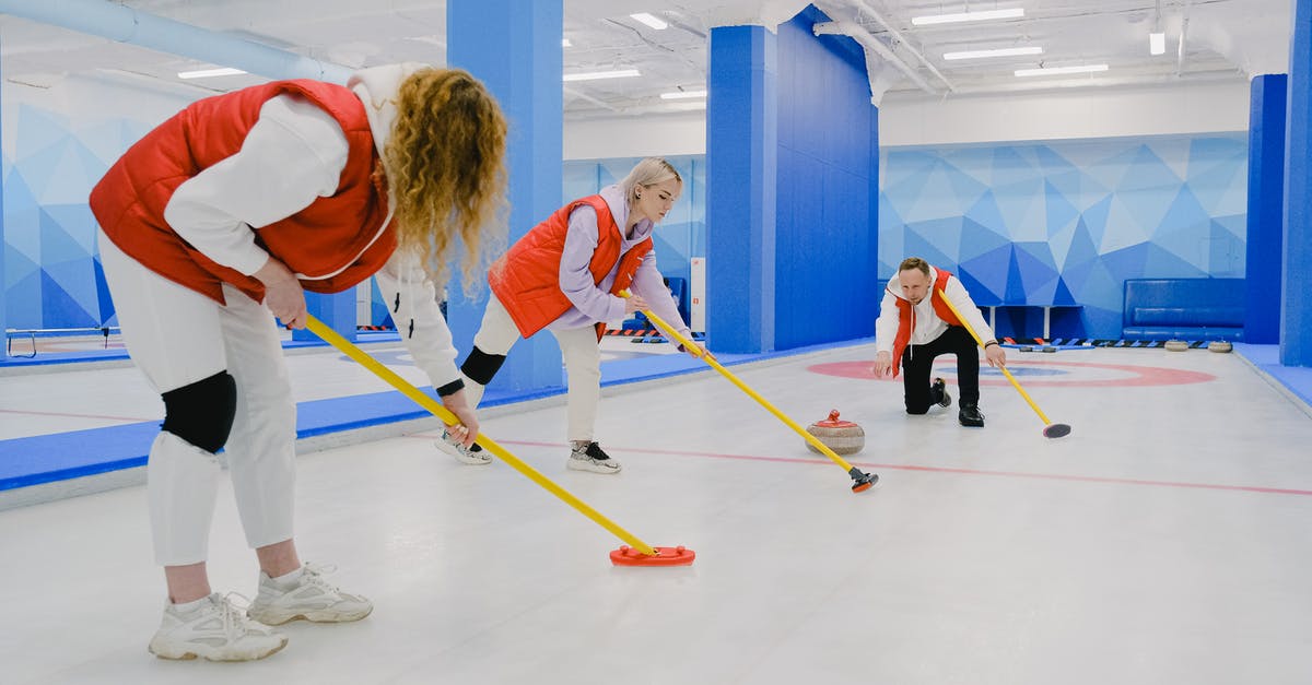Playing a game, what measurement of speed is u/s? - Full body of sportsman throwing curling stone near sportswomen in activewear sweeping ice sheet with special brooms while playing game