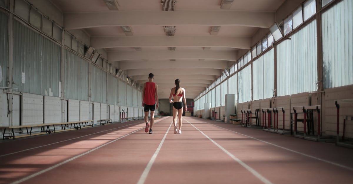 Power up while running - Back view of sportsman and sportswoman in activewear walking along running track in athletics arena during warming up before training Power up while running - Back view of sportsman and sportswoman in activewear walking along running track in athletics arena during warming up before training