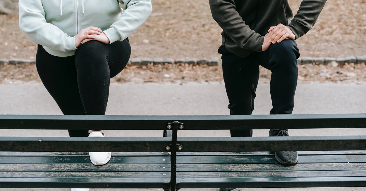 Power up while running - Crop faceless fit man and overweight woman putting legs on wooden bench while training together in autumn park Power up while running - Crop faceless fit man and overweight woman putting legs on wooden bench while training together in autumn park